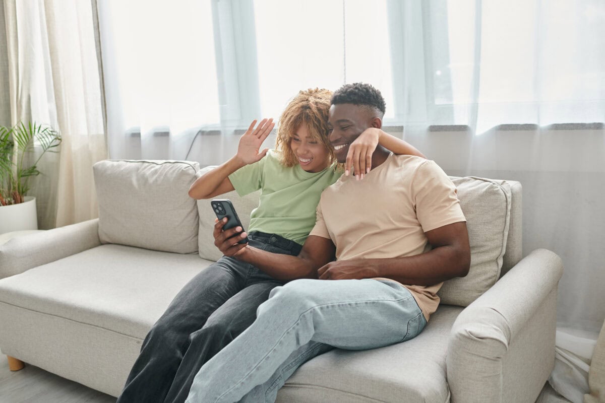 Happy african american couple video chatting on a smartphone while sitting on couch together